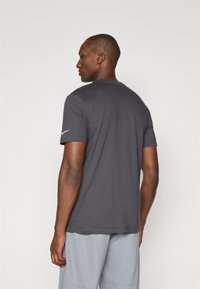 Grå atletisk t-shirt med korte ærmer, lavet af glat stof, med et minimalistisk design og et lille hvidt logo på venstre ærme.