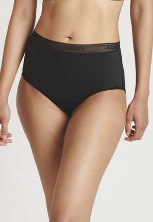 Frau in schwarzen hochgeschnittenen Slips mit einem Markenbund, von der Taille bis zur Mitte des Oberschenkels vor einem schlichten Hintergrund dargestellt.