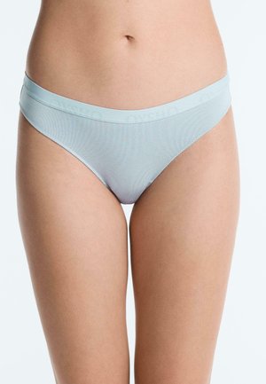 Žena nosi svetlomodré bavlnené spodné prádlo vo štýle bikín s výrazným pásom, zobrazená od oblasti brucha po hornú časť stehien.