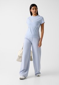 Jasnoniebieski zestaw składający się z topu z krótkim rękawem i szerokich spodni, wykonany z gładkiej tkaniny. Na topie znajduje się białe logo.