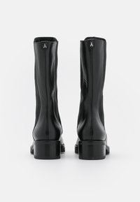 Botas de tobillo de cuero negro con textura suave, con puntera redonda, tacón cuadrado y acento de logo en el cierre con cremallera.