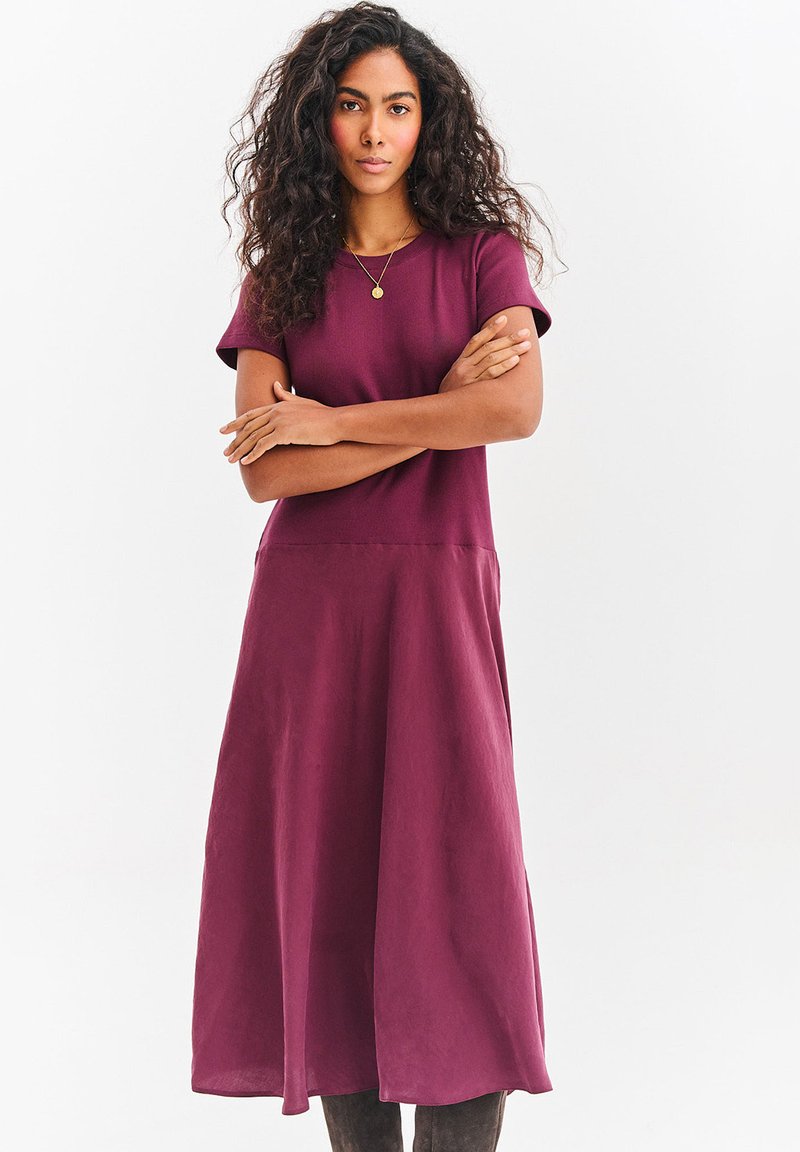 Sukienka do kolan w głębokim bordowym kolorze, z krótkimi rękawami i luźnym krojem, o gładkiej fakturze i zwiewnej spódnicy.