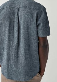 Camicia a maniche corte in tessuto blu scuro con trama a griglia sottile, orlo arrotondato e piega centrale sul retro.