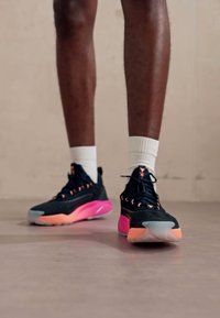 Scarpe da ginnastica nere con tomaia testurizzata e accenti rosa. Presentano una suola imbottita con dettagli in gradiente di blu chiaro e rosa.