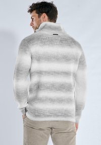 Grau-weiß gestreifter Pullover mit hohem Kragen, gerippter Struktur und einem Etikett am Rücken. Hergestellt aus weichem, gestricktem Material.