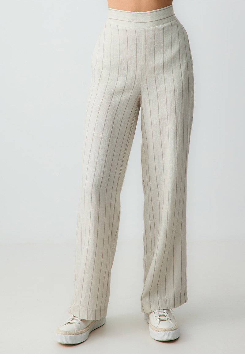 Linnenmix broek met wijde pijpen in lichtbeige met verticale strepen. Beschikt over een hoge taille en een relaxte pasvorm, gecombineerd met witte sneakers.