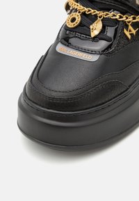 Baskets à plateforme noires avec chaîne dorée et breloques, ornées de finitions en cuir verni et du logo « Karl Lagerfeld » sur l'avant.