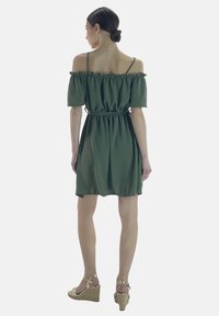 Vestido verde oliva sin hombros con mangas con volantes, cintura ceñida y falda acampanada. Llevado con sandalias de cuña beige.