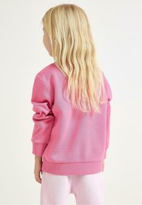 Rosa Sweatshirt mit rundem Ausschnitt und gerippten Bündchen, mit einer glatten Textur. Kombiniert mit hellrosa Leggings.