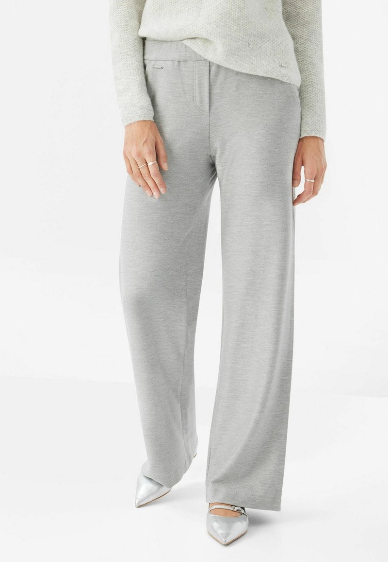 Pantalon gris à jambes larges en tissu doux, doté d'une ceinture élastique, de poches latérales discrètes, et assorti à des chaussures argentées à bout pointu et brillantes.