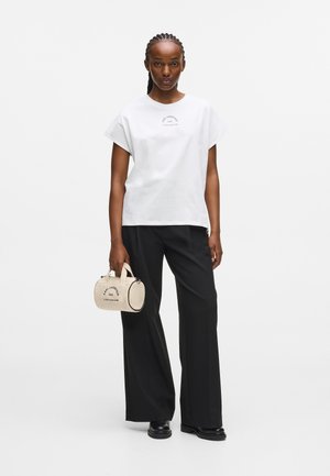 Hvit kortermet t-skjorte med rund halslinning og trykt logo. Svart vide bukser. Liten beige veske med topphåndtak og logo-detalj.