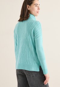 Pull en maille turquoise avec col haut, présentant un motif texturé et un ourlet côtelé. Manches longues avec une coupe décontractée.