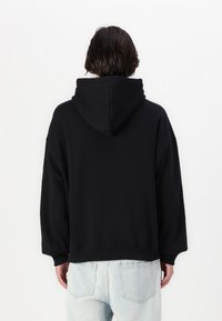 Svart hooded sweatshirt med lös passform, ribbade ärmslut och fåll. Har en känguruficka. Bärs med ljusblå jeans.