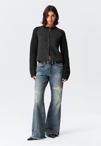Zwarte wollen cardigan met knoopsluiting, gecombineerd met distressed blauwe denim flared jeans. Accentueert met een zwarte riem en punten-schoen.