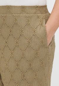 Χακί παντελόνι με floral διαμαντένιο σχέδιο, φτιαγμένο από υφή υφάσματος. Περιέχει τσέπες και καλή εφαρμογή στη μέση. Ορατές περίπλοκες κοπές.