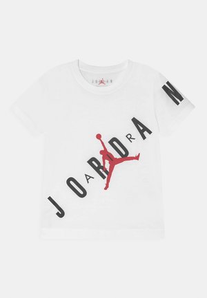 T-shirt bianca a maniche corte con grande scritta nera "JORDAN" e logo Jumpman rosso diagonale sul davanti, e una "N" nera sulla manica destra.