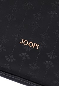 Czarna torebka kopertówka o fakturowanej powierzchni z subtelnym kwiatowym wzorem, z błyszczącym, złotym akcentem logo "JOOP!" na środku.