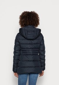 Kurtka puchowa w ciemnym granacie, z poziomym pikowanym wzorem, kapturem i elastycznymi mankietami. Materiał ma gładką, błyszczącą teksturę.