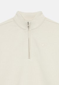 Svetlo béžová pulóver so štvrť zipsom vyrobený z jemnej látky. Má strieborný zips a malé vyšívané logo na ľavom prsníku.