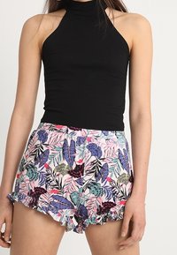 Haut à bretelles noir associé à un short floral multicolore avec ourlet à volants, principalement rose avec des motifs de feuilles violettes et vertes.