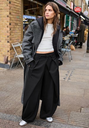 Grey wool overcoat with a black hood, white crop top, and wide black trousers. Silver shoes, relaxed fit, and pleated design.