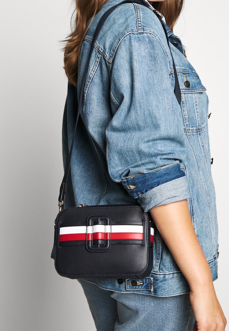 Small black leather crossbody bag featuring a rectangular shape, zip closure, and red and white stripe accents on the front.