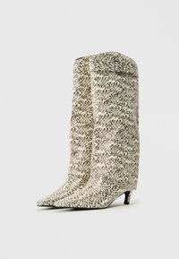 Puntige enkelboots met een textuur van crème en zwart patroon. Hoge schacht, een lichte hak en een gespaccent aan de bovenkant.