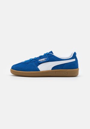 Blå Puma Palermo sneaker med hvid stribe, gummisål og snørebånd, vist fra siden på hvid baggrund.