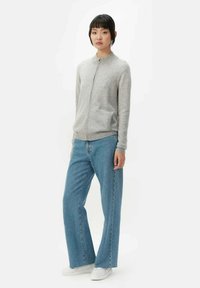 Grå zip-up stickad cardigan med rund halsringning och två framfickor, i kombination med ljusblå vida jeans och vita sneakers.