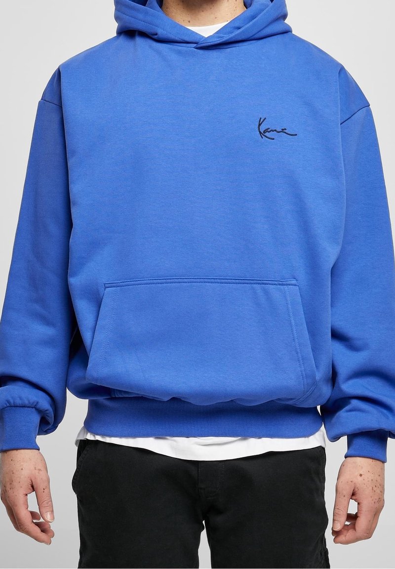 Sudadera con capucha azul de tela suave, con un bolsillo frontal estilo canguro, puños acanalados y un pequeño logo negro en el pecho.