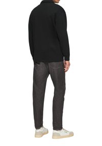 Schwarzes Langarm-Polohemd kombiniert mit dunkelgrauen Jeans und weißen Sneakers. Das Material ist Baumwolle, was einen lässigen Look verleiht.