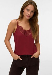 Marmoreret camisole med blonde detaljer langs halsudskæringen. Glat stof med tynde stropper. Båret med brune fløjl bukser, hænderne i lommerne.