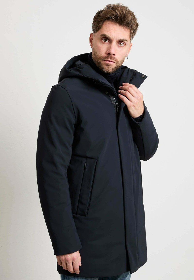 Marineblauwe parka met capuchon, voorzien van een rits aan de voorkant, drukknoopsluiting en zijzakken. Gladde stof met een strak ontwerp.