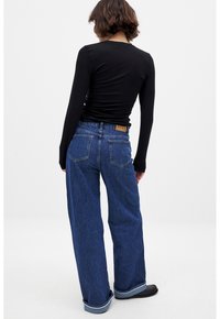 Top negro de manga larga combinado con unos jeans azules de tiro alto y pierna ancha. Los jeans tienen un parche de cuero y bolsillos traseros con detalles de costura.