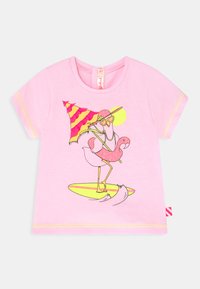 T-shirt rosa de manga curta com uma ilustração de tema de praia de um flamingo em uma prancha de surf, segurando óculos de sol e um guarda-sol, detalhada em cores vivas.