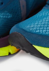 Zapatillas deportivas azules con parte superior de malla texturizada, que cuentan con una suela de goma negra y acentos amarillos brillantes en el talón. Diseño ligero.