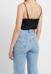 Schwarzes Satin-Camisole mit Spitzendetails, kombiniert mit hochgeschnittenen hellblauen Jeans aus Denim mit Gesäßtaschen und einem Lederlabel.