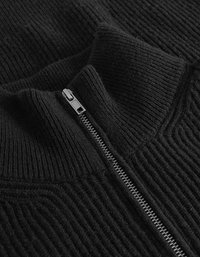 Μαύρος πλεκτός πουλόβερ με ψηλό γιακά, διαθέτει μπροστινό φερμουάρ και κατακόρυφη ραβδωτή υφή. Το ύφασμα φαίνεται μαλακό και ζεστό.