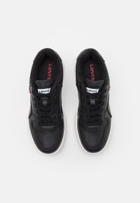 Baskets en cuir noir avec une semelle en caoutchouc blanche. Les caractéristiques incluent un col rembourré, des lacets noirs et un logo blanc Levi's sur la languette.