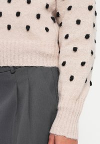 Maglione lavorato a maglia rosa chiaro con pois neri a pallini. Polsini e orlo a costine. Abbinato a pantaloni grigio scuro, che evidenziano una vestibilità rilassata.
