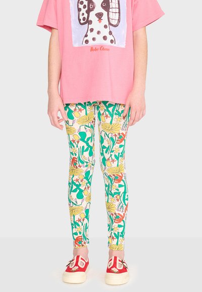 Enfant portant un t-shirt rose avec un motif de chien, des leggings à motif floral et des chaussures faciles à enfiler rouges avec des semelles blanches.