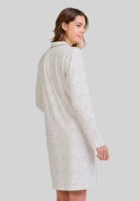Vestido de color crema con lunares azul marino y dorados, de manga larga, con cuello y un corte relajado, que presenta un largo hasta la rodilla y una textura suave.