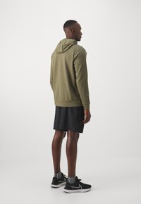 Sudadera verde oliva con capucha, tela texturizada, diseño ajustado, combinada con pantalones cortos negros y zapatillas deportivas negras. Look simple y funcional.