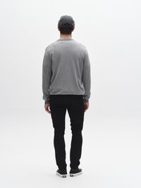 Siva majica dugih rukava, crne hlače i crne tenisice. Model prikazan s leđa, stoji nasuprot jednobojnoj bijeloj pozadini.