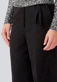 Black wide-leg pants feature a soft texture, a drawstring waist, and are paired with a sparkling silver and black sequined top.