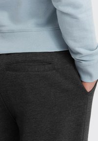 Lichtblauwe sweatshirt met ribbels aan de mouwen en onderkant, gecombineerd met donkergrijze sweatpants met een achterzak en zachte, gestructureerde stof.