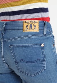 Vaqueros de denim azul con un diseño de cinco bolsillos, que presentan costuras en contraste, una etiqueta de piel marrón con el logo y una silueta ajustada.