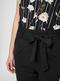 Black trousers with a tied belt detail at the waist. The fabric appears smooth, and a floral top with vertical stripes is partially visible.