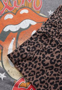 Szürke póló, narancs és fehér Rolling Stones logóval; barna szövet fekete leopárdmintával, amely részben átfedi a pólót.