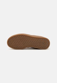Suela de zapato de goma marrón con un patrón texturizado de pequeños diamantes, con forma redondeada y un logo grabado cerca del talón.